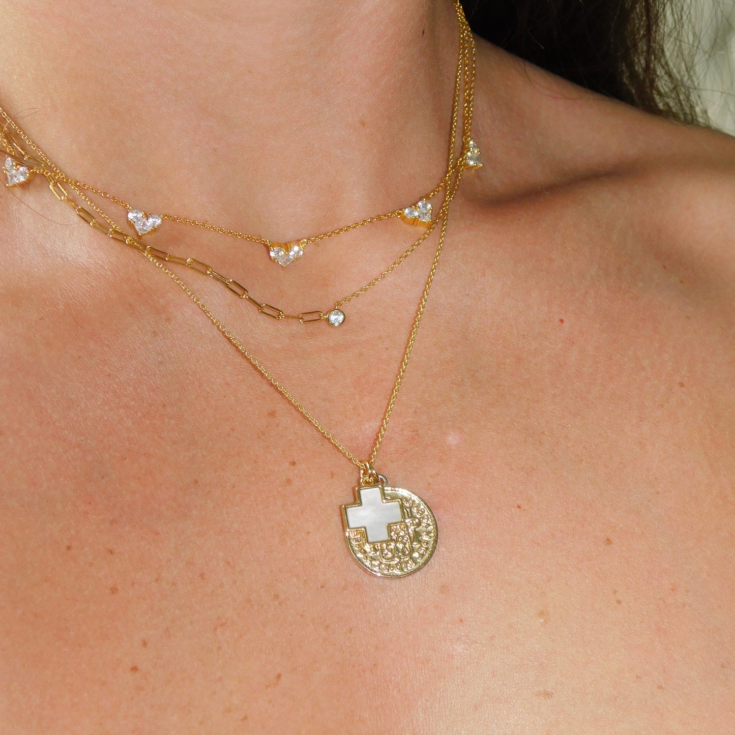 Gold body chain with a circular pendant featuring a cross on a person's shoulder.